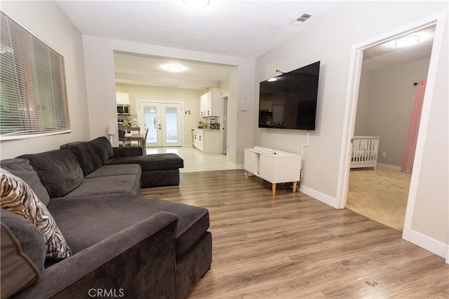 living room featuring light wood-style floors, french doors, visible vents, and baseboards