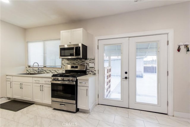 kitchen featuring tasteful backsplash, appliances with stainless steel finishes, light countertops, french doors, and a sink