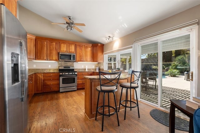 kitchen featuring lofted ceiling, stainless steel appliances, wood finished floors, and brown cabinets