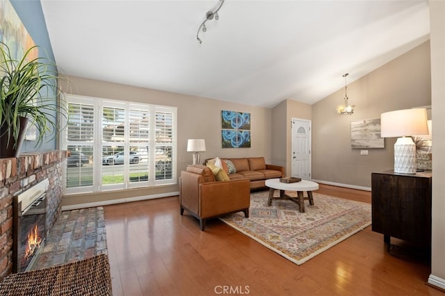 living area featuring lofted ceiling, a glass covered fireplace, track lighting, wood finished floors, and baseboards