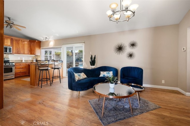 living area with lofted ceiling, baseboards, light wood finished floors, and ceiling fan with notable chandelier