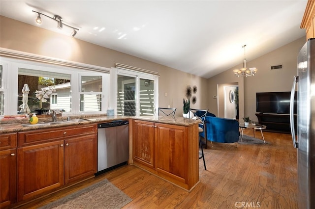 kitchen with stainless steel appliances, lofted ceiling, a sink, and wood finished floors