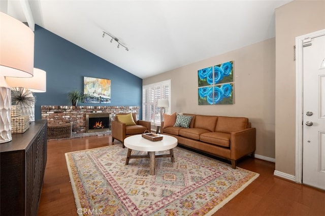 living area with lofted ceiling, a brick fireplace, baseboards, and wood finished floors