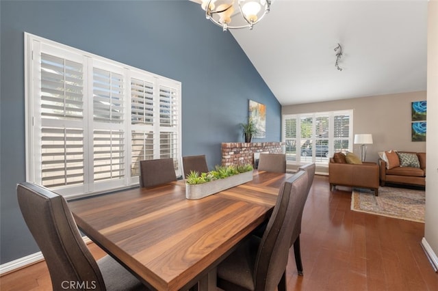 dining space with baseboards, wood finished floors, rail lighting, high vaulted ceiling, and a notable chandelier