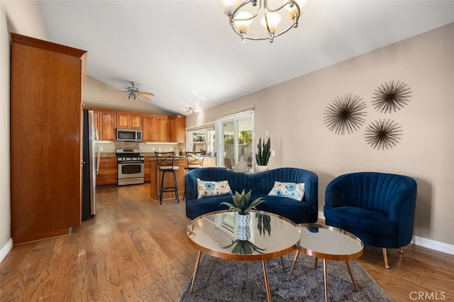 living room featuring lofted ceiling, ceiling fan with notable chandelier, light wood-style flooring, and baseboards