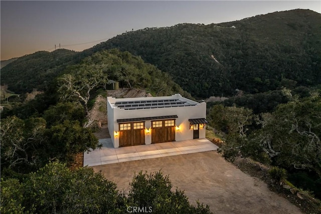 back of property at dusk featuring a mountain view, driveway, and stucco siding