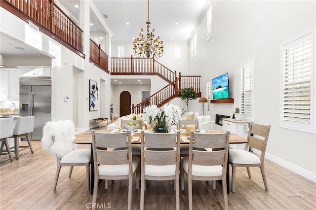 dining space featuring light wood-style flooring, a chandelier, baseboards, a fireplace, and a high ceiling