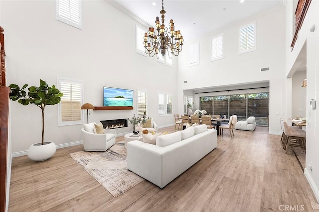 living area featuring light wood-type flooring, baseboards, a glass covered fireplace, and a chandelier