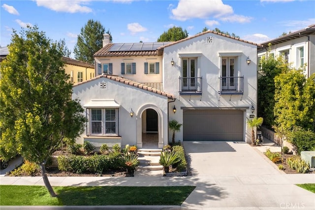 mediterranean / spanish-style house with an attached garage, a balcony, solar panels, concrete driveway, and stucco siding