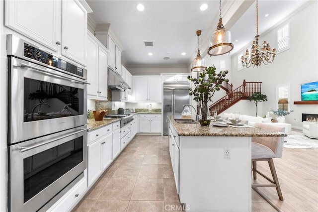 kitchen featuring under cabinet range hood, visible vents, a sink, crown molding, and appliances with stainless steel finishes