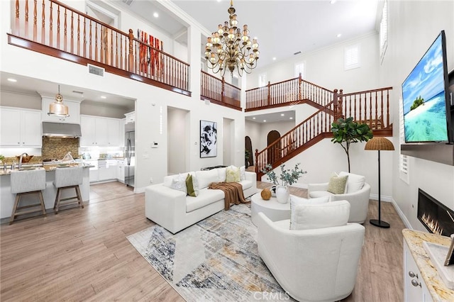 living room featuring light wood-style floors, stairs, a warm lit fireplace, and crown molding