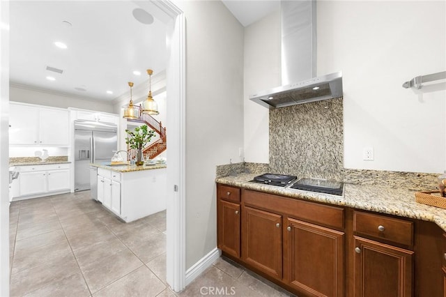 kitchen featuring wall chimney exhaust hood, stainless steel built in refrigerator, light tile patterned flooring, backsplash, and light stone countertops