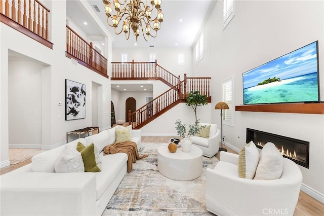 living area with baseboards, a glass covered fireplace, a towering ceiling, wood finished floors, and stairs