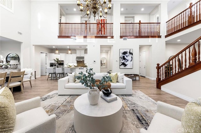 living room featuring a towering ceiling, an inviting chandelier, visible vents, light wood-type flooring, and baseboards