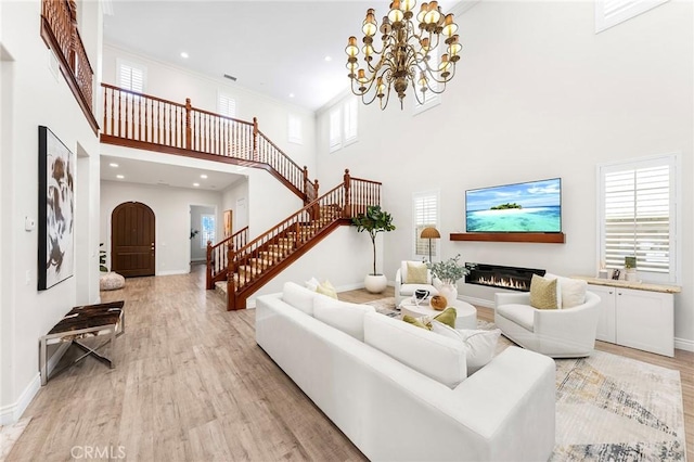 living room featuring a glass covered fireplace, light wood-style floors, a high ceiling, and stairs