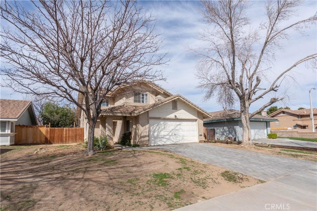 traditional-style house featuring a garage, fence, decorative driveway, and stucco siding