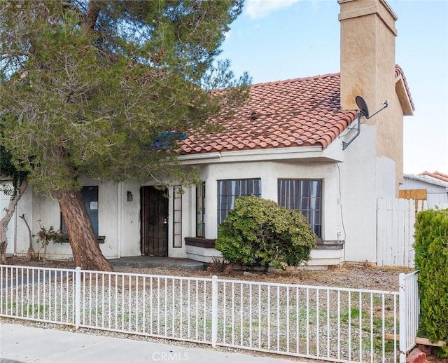 view of front facade with a tiled roof, a chimney, a fenced front yard, and stucco siding