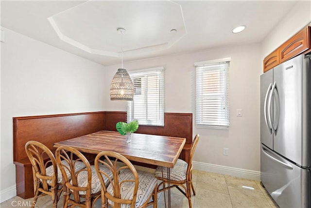 dining space featuring light tile patterned floors, a tray ceiling, breakfast area, and baseboards