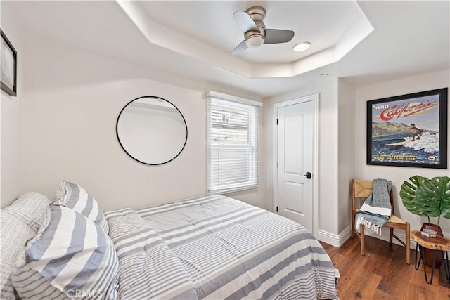 bedroom with a ceiling fan, a tray ceiling, baseboards, and wood finished floors