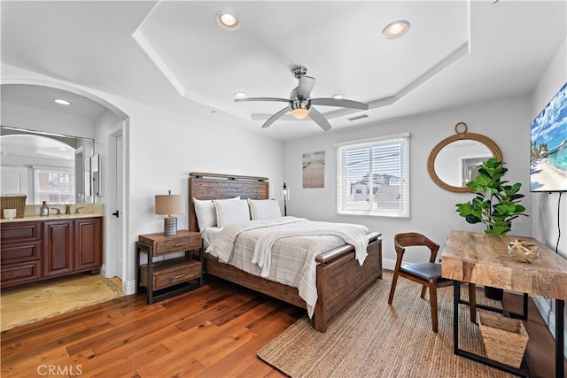 bedroom featuring light wood-type flooring, multiple windows, a tray ceiling, and recessed lighting