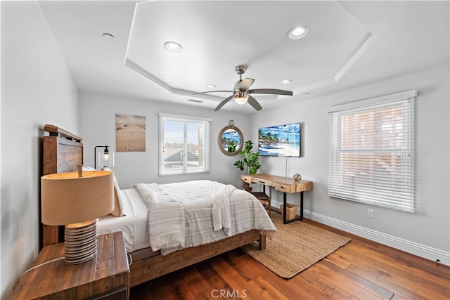 bedroom featuring a tray ceiling, recessed lighting, hardwood / wood-style floors, and baseboards