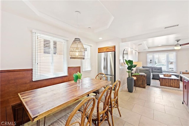 dining space with visible vents, a raised ceiling, wainscoting, ceiling fan, and light tile patterned flooring