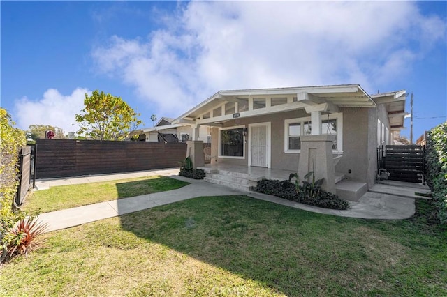 view of front of home featuring covered porch, a front yard, fence private yard, and stucco siding