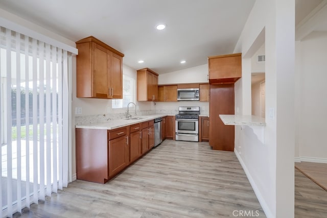 kitchen featuring brown cabinetry, light wood-style floors, stainless steel appliances, and a sink