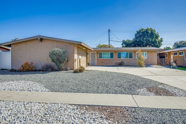 ranch-style home featuring driveway, an attached garage, fence, and stucco siding