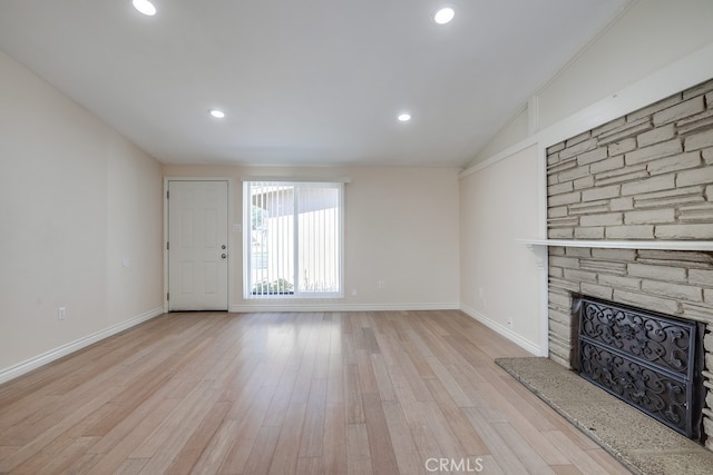 unfurnished living room with lofted ceiling, a stone fireplace, baseboards, and light wood-style floors