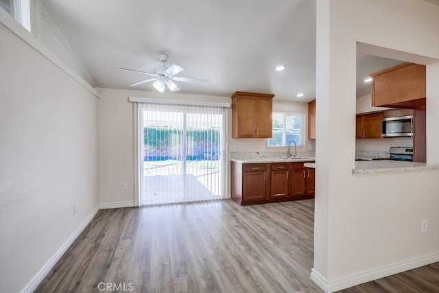 kitchen featuring light wood finished floors, baseboards, appliances with stainless steel finishes, brown cabinets, and a sink