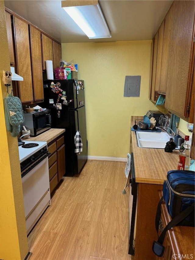 kitchen featuring light wood finished floors, electric range, freestanding refrigerator, a sink, and under cabinet range hood