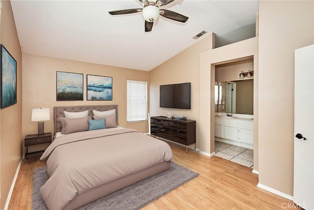 bedroom featuring light wood finished floors, lofted ceiling, visible vents, ensuite bathroom, and baseboards