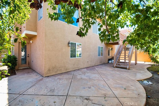 back of house featuring stairway, a patio area, and stucco siding