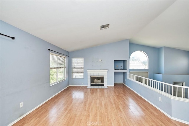 unfurnished living room featuring a fireplace, visible vents, vaulted ceiling, wood finished floors, and baseboards