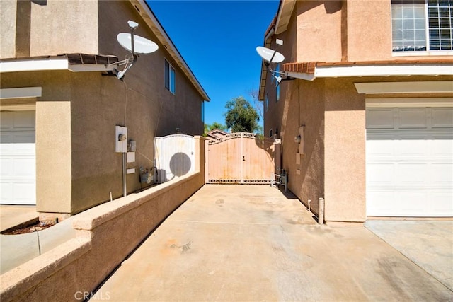 view of side of property with a garage, a gate, and stucco siding