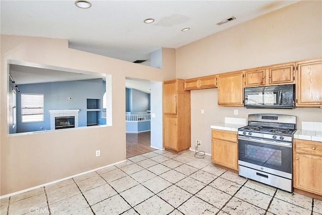 kitchen featuring visible vents, a tiled fireplace, tile countertops, black microwave, and gas stove