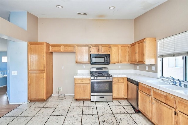 kitchen featuring visible vents, tile counters, stainless steel appliances, high vaulted ceiling, and a sink