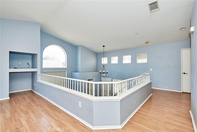 hallway featuring a chandelier, wood finished floors, visible vents, and baseboards