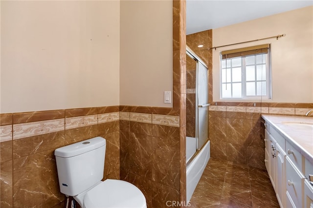 bathroom featuring a wainscoted wall, toilet, marble finish floor, tile walls, and vanity