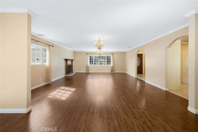 unfurnished living room with a notable chandelier, wood finished floors, arched walkways, crown molding, and baseboards