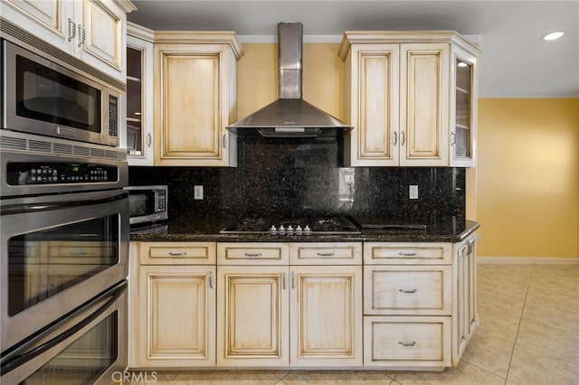 kitchen featuring light tile patterned flooring, stainless steel appliances, cream cabinetry, wall chimney exhaust hood, and tasteful backsplash