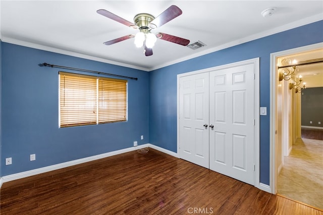 unfurnished bedroom with visible vents, crown molding, baseboards, wood finished floors, and a closet