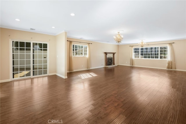 unfurnished living room with wood finished floors, baseboards, an inviting chandelier, a fireplace with raised hearth, and crown molding