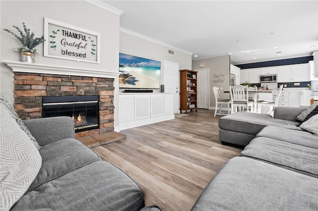 living area featuring light wood-type flooring, visible vents, a stone fireplace, crown molding, and baseboards