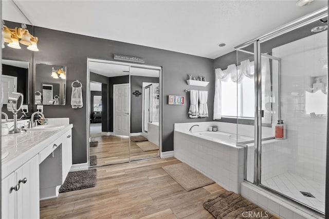 bathroom with a stall shower, wood finished floors, baseboards, a bath, and vanity