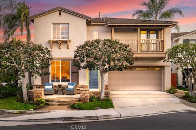 view of front of home with a balcony, driveway, an attached garage, stucco siding, and stone siding