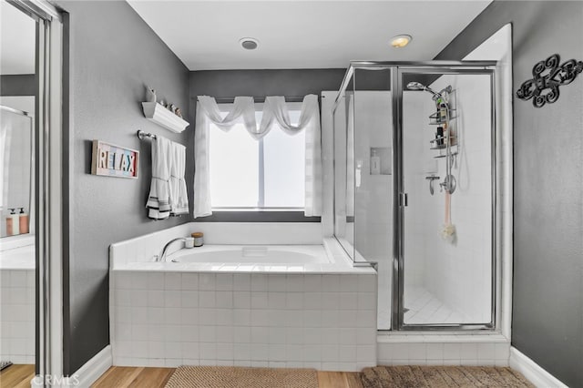 bathroom with a shower stall, a garden tub, wood finished floors, and baseboards