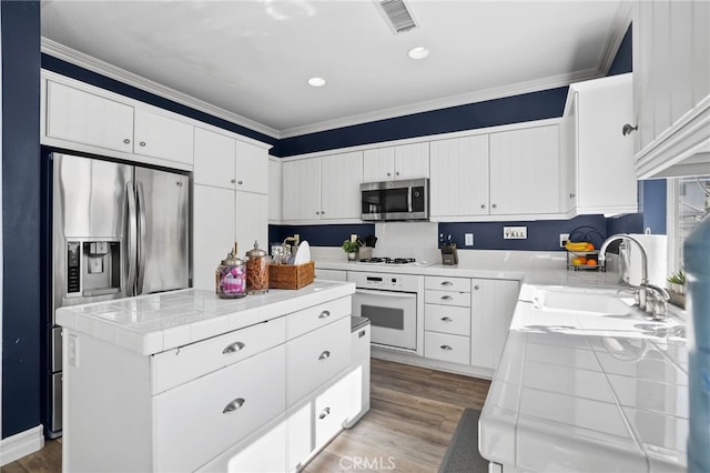 kitchen with visible vents, a sink, tile counters, appliances with stainless steel finishes, and light wood-type flooring