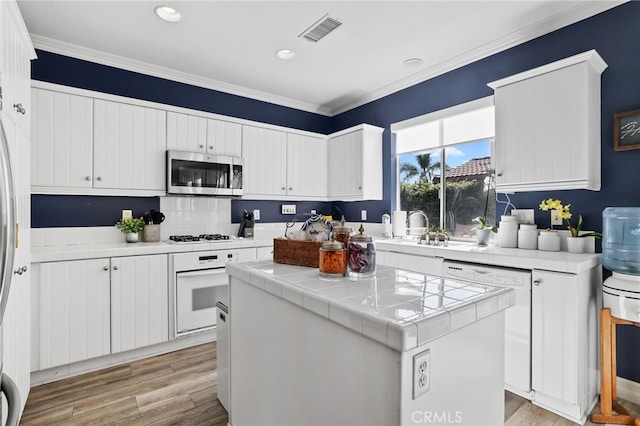 kitchen featuring visible vents, tile counters, light wood-style floors, white appliances, and a sink